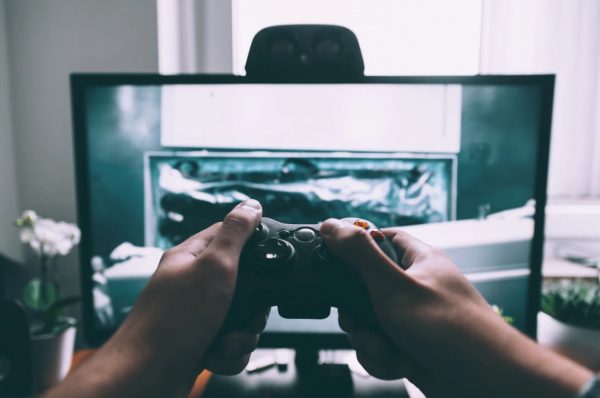 A person holding a game controller in front of a PC monitor.