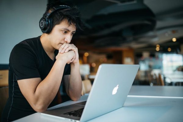 A guy wearing a wireless headset while staring at a macbook screen.