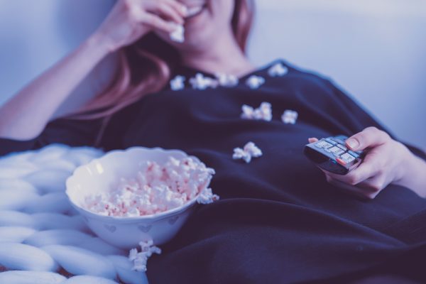 How to download movies on Hulu Lady in black dress watching television while eating popcorn.