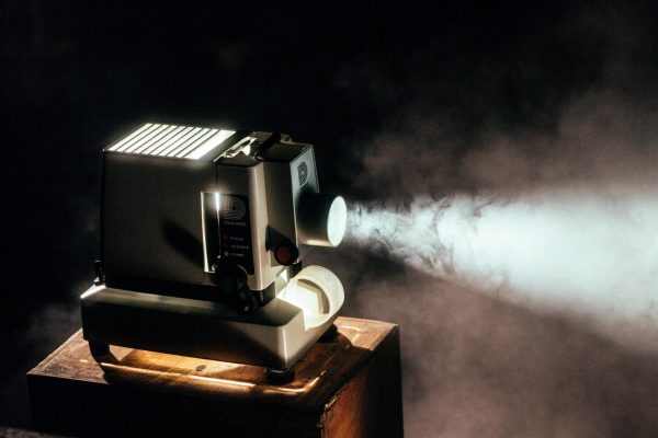 Photo of a movie projector projecting light onto something, while it’s on top of a wooden table with white smoke around and a youtube free movies