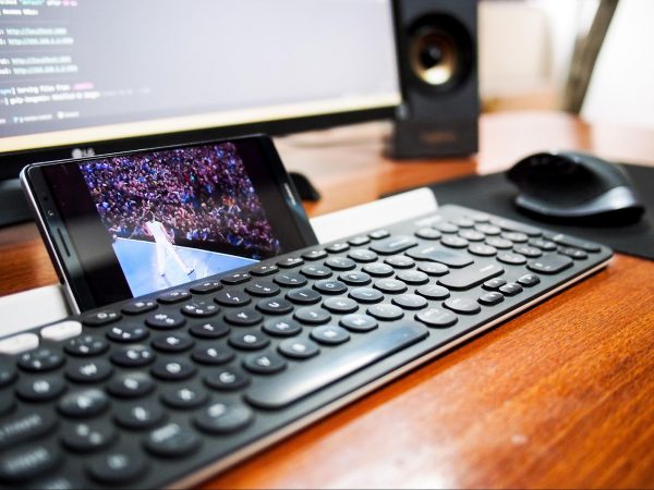 watch youtube free movies a concert in front of a crowd, the phone is upright against a keyboard with a monitor in front and a mouse to the right, all on a wooden table