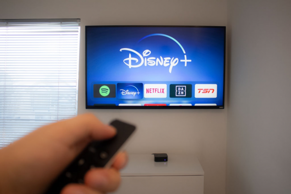 erson holds an Apple TV remote using the new Disney+ app on a Vizio TV